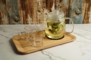 Clear glass teapot with herbal tea and matching cups on a wooden tray.